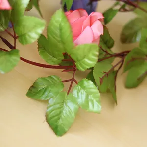 Nahaufnahme grüner Seidenblätter und pinker Blüte einer künstlichen Rosenrebe zur Dekoration