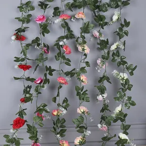 Multi-colored artificial rose garlands with green leaves hanging against gray wall