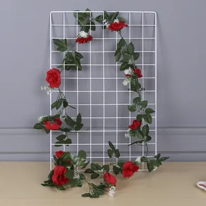 Artificial red rose vine wrapped around a white metal grid panel for home decor