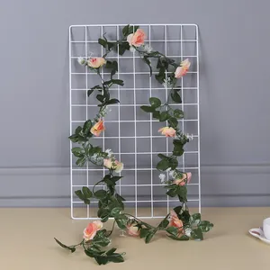 Artificial pink rose garland with green leaves draped on a white metal wire grid panel