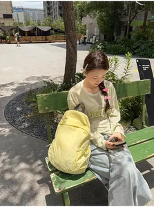 Lightweight yellow minimalist backpack for women shown in a lifestyle park setting
