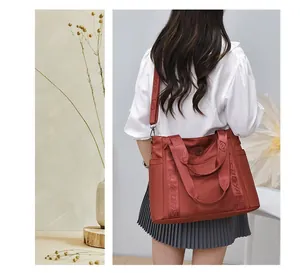Modella con camicetta bianca che porta a spalla una grande borsa da viaggio rosso mattone
