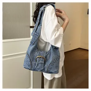 Detail showing a denim motorcycle-style hobo bag with rivets and metal buckle on a model.