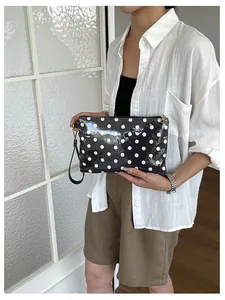 A stylish black and white polka dot travel makeup bag shown in a handheld lifestyle setting