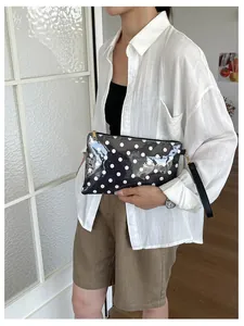 Detailed view of the black and white polka dot cosmetic bag held by a model in a linen shirt