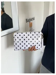 Detail view of a white polka dot makeup bag with a gold zipper and wrist strap.