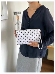 Close-up of a stylish white polka dot cosmetic bag with wristlet held by a person