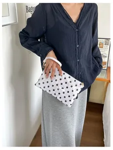Detail shot of a stylish white polka dot cosmetic bag held by a model for scale.