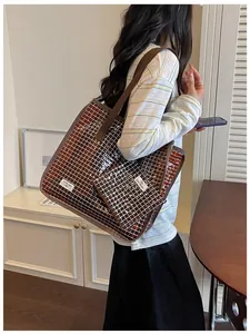 Dettaglio di una borsa tote in PVC a scacchi marroni indossata da una modella in interno