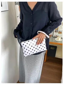 Handheld white travel cosmetic bag with black polka dots and wrist strap