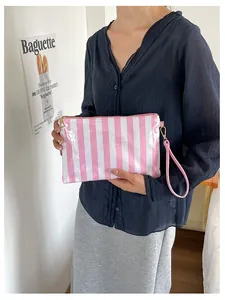 Pink and white striped portable cosmetic bag held by a model in a clean indoor setting
