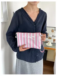 Detail view of a pink and white striped travel cosmetic bag held by a fashion model