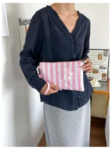 Detail view of the pink and white striped cosmetic bag held by a model in a room