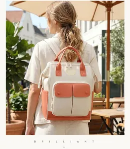 Back view of a stylish cream and orange diaper bag backpack worn by a model outdoors