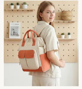 Multi-functional beige and orange diaper backpack shown worn by a model in a lifestyle setting.