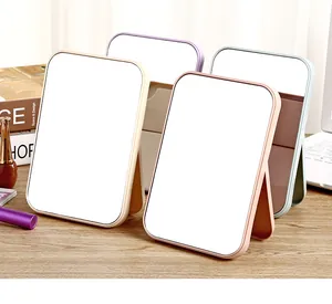 Pastel colored foldable desktop makeup mirrors arranged on a natural wooden desk surface.