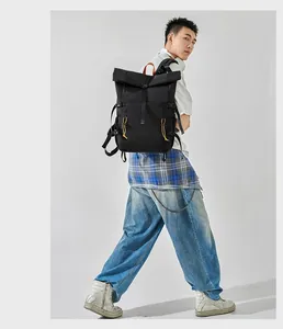 Stylish black roll-top backpack worn by a model in a casual business street style look.