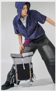 Detailed shot of a stylish gray and black roll-top backpack held by a male model.