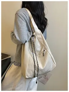 Vue latérale d'un grand sac à cordon crème porté par un modèle dans un cadre épuré.