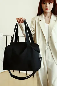 Model carrying a large black nylon travel bag with top handles and shoulder strap