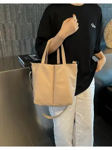 Close-up of a beige minimalist crossbody tote bag worn by a model in a modern room.