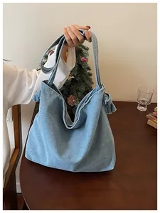 Detailed view of light blue denim tote bag featuring side knot design on a wooden table