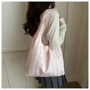 Detail view of a pink and white striped tote bag with bow pattern carried by a model