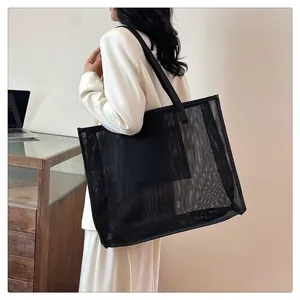 Bolso shopper grande de malla de nailon negro llevado por una modelo en estudio.