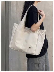 Side view of large cream nylon tote bag with multi-pocket design on model's shoulder.