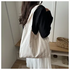 Detailed view of a cream striped tote bag worn by a model in a minimalist setting