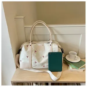 Large travel duffle bag with floral embroidery and green tablet prop on wooden table