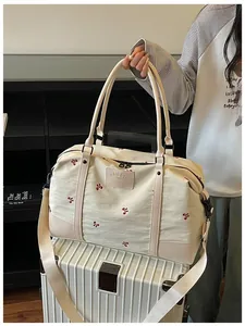 Cream travel bag with red flower embroidery presented on top of a white suitcase