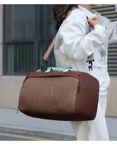 Model carrying a large capacity brown checkered duffel bag for travel or gym use