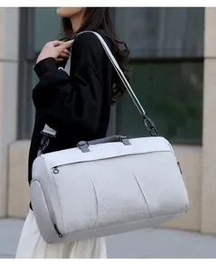 Model carrying a large grey travel duffle bag with shoulder strap in an urban outdoor setting