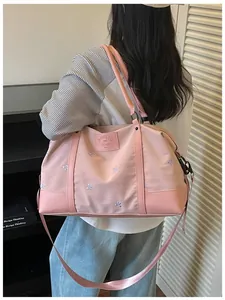 Back view of a model carrying a large pink expandable travel bag with bow embroidery