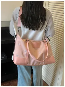 Large pink expandable travel bag with bow embroidery carried by a female model outdoors