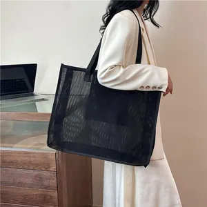 Bolso de malla negro de gran capacidad para compras y playa, colgado al hombro de modelo.