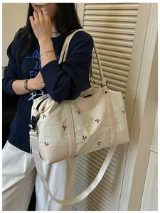 Large capacity cream travel bag with red bow embroidery shown on shoulder