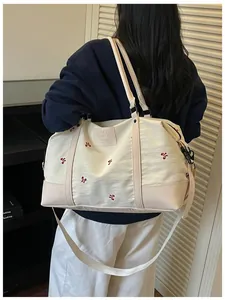 Detailed view of a model carrying a large cream travel bag with red bow embroidery