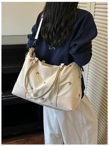 Cream large capacity travel bag with red embroidery details shown carried on shoulder