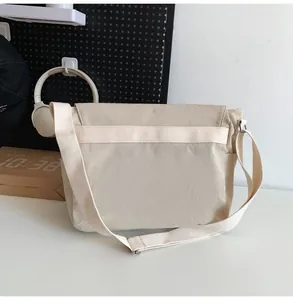 Minimalist beige canvas messenger bag shown from a clean back-side studio angle.