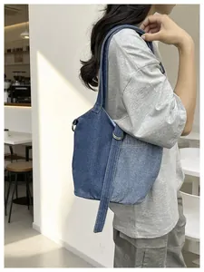 Gros plan d'un sac seau en jean bleu porté à l'épaule dans un café au style épuré