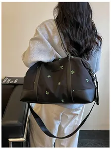 Macro view of a large black duffle bag featuring green bow embroidery and carrying strap.