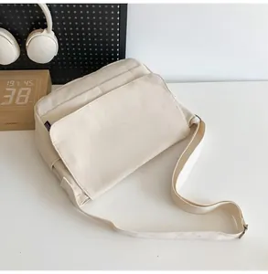 Close-up of a minimalist cream canvas messenger bag with adjustable strap on a desk