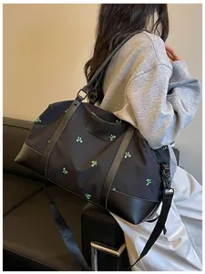 Detailed side view of a large black travel bag featuring green embroidered bow patterns on model shoulder.