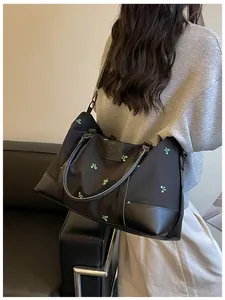 Large black travel bag with green embroidery worn over the shoulder by a woman.