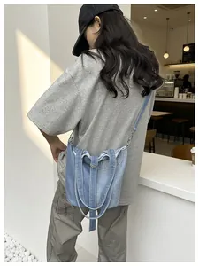 Sac seau en jean bleu élégant porté en bandoulière dans un café au décor moderne.