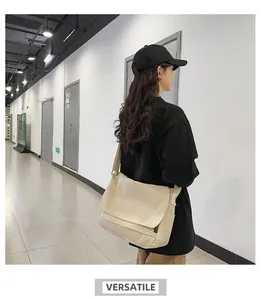Woman wearing a large beige canvas messenger bag in a minimalist indoor setting