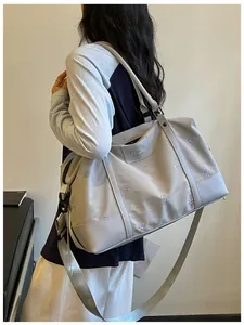 Close-up of a lightweight grey travel bag with purple bow embroidery carried by a model.