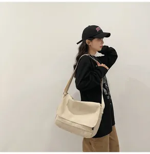 Model wearing a large cream canvas messenger bag in a minimalist streetwear style